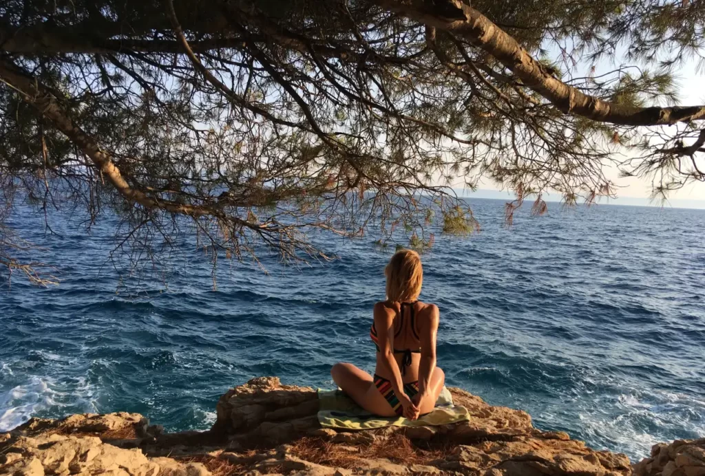 Romana sjedi na stijeni na moru s isprepletenim rukama iza leđa